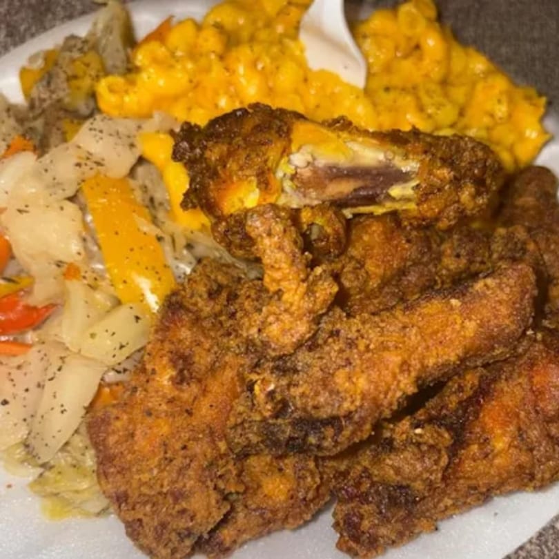 Crispy fried chicken, mac and cheese, and seasoned cabbage on a white plate.