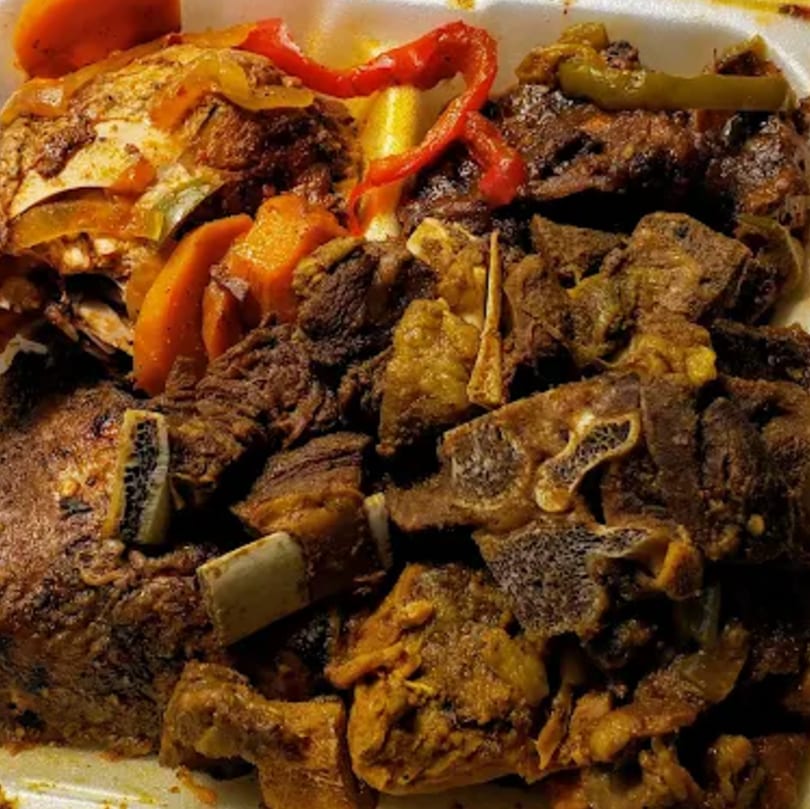 A close-up of Jamaican curry goat and brown stew chicken with peppers and carrots.