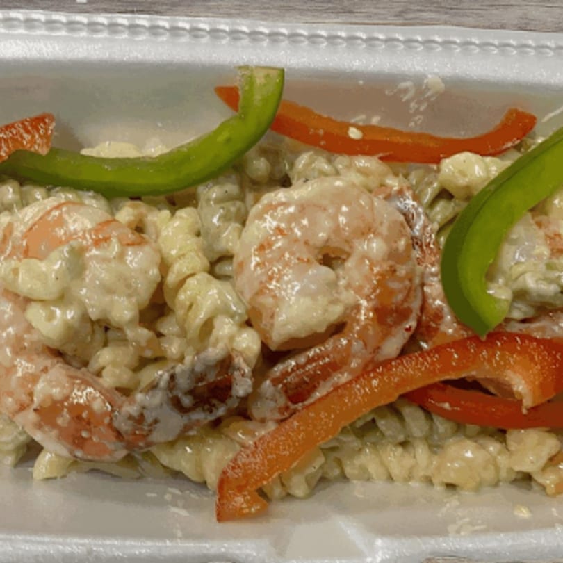 Creamy pasta with shrimp, red and green bell peppers in a white takeout container.