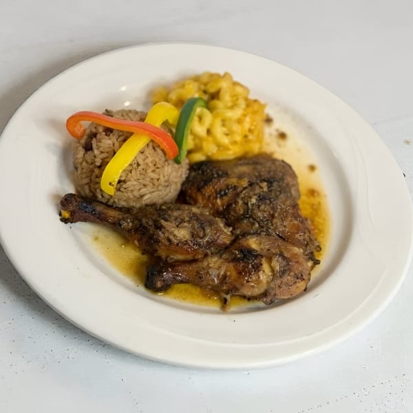 A plate of Jamaican jerk chicken with rice and peas, topped with bell peppers, and a side of macaroni and cheese.