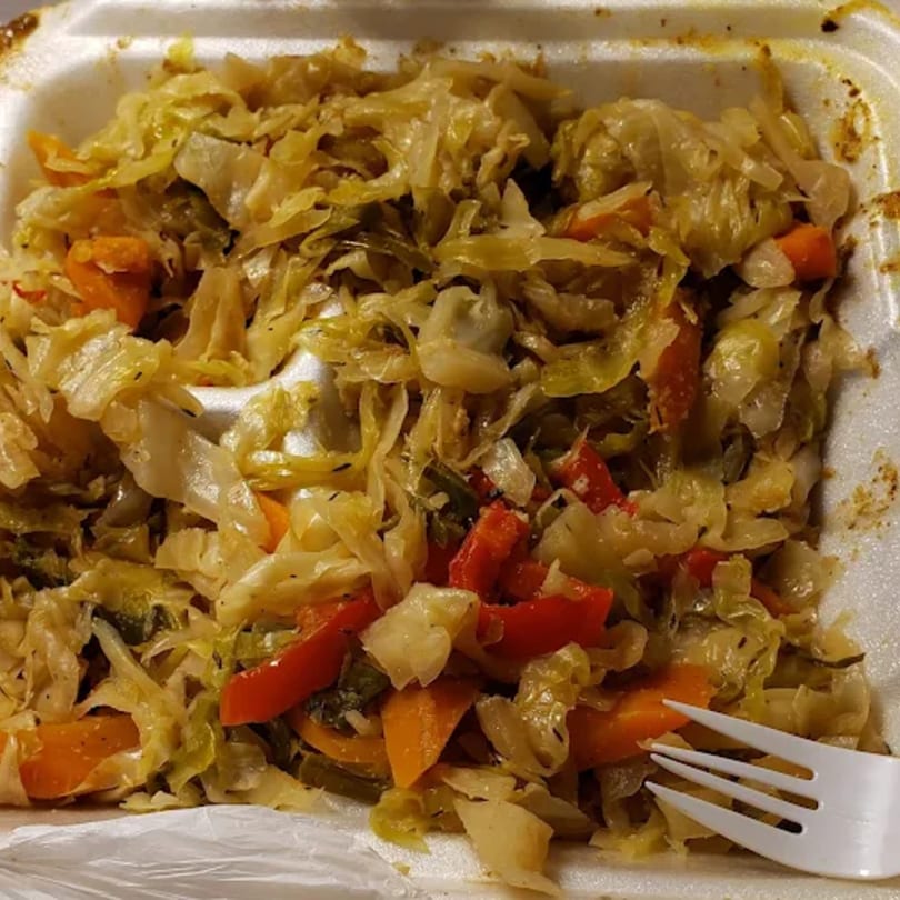 A close-up of Jamaican steamed cabbage with carrots and peppers in a white takeout container.