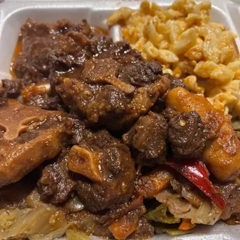 A close-up of Jamaican oxtail stew with macaroni and cheese and mixed vegetables.